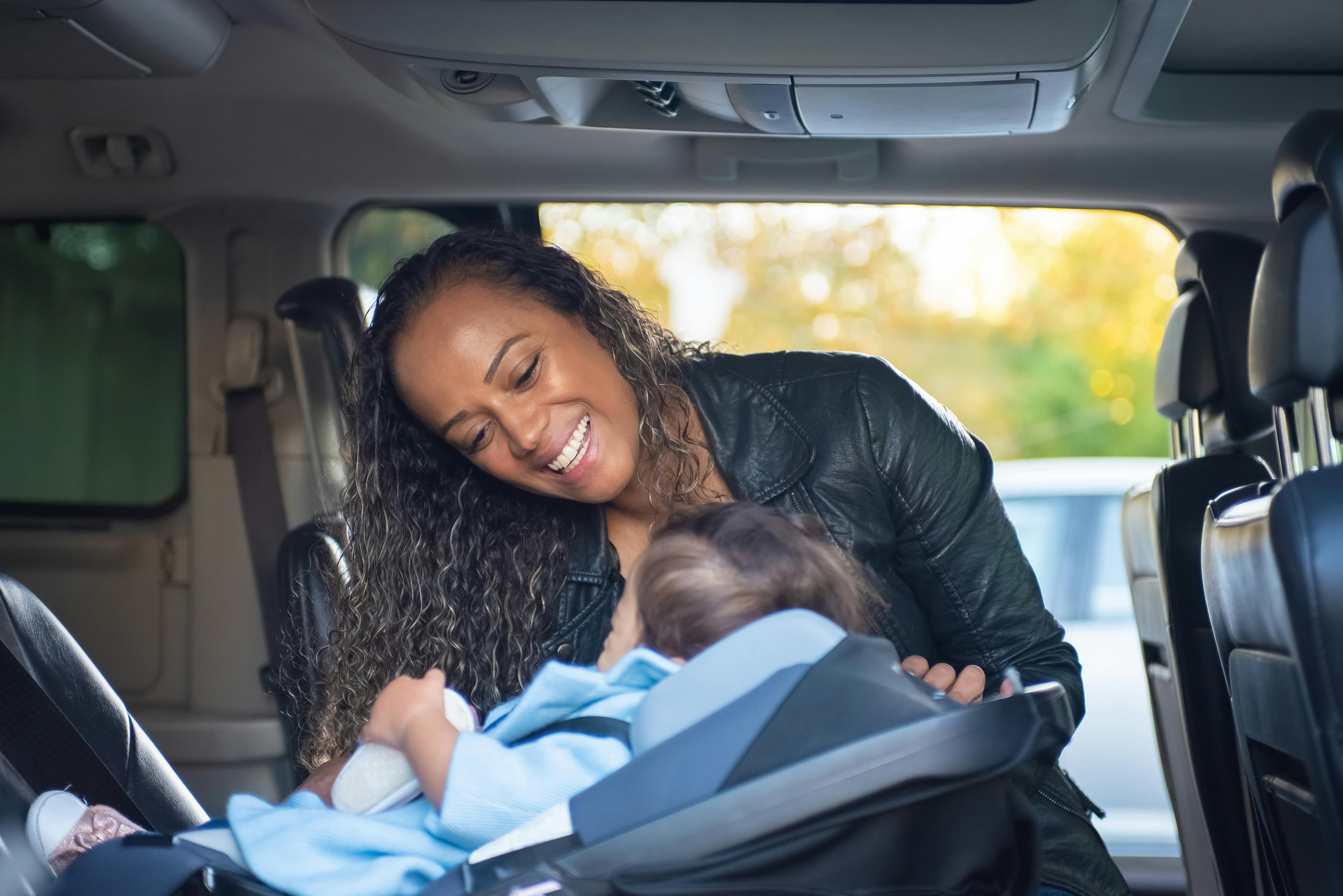 Mother smiling while placing infant into a rear-facing car seat