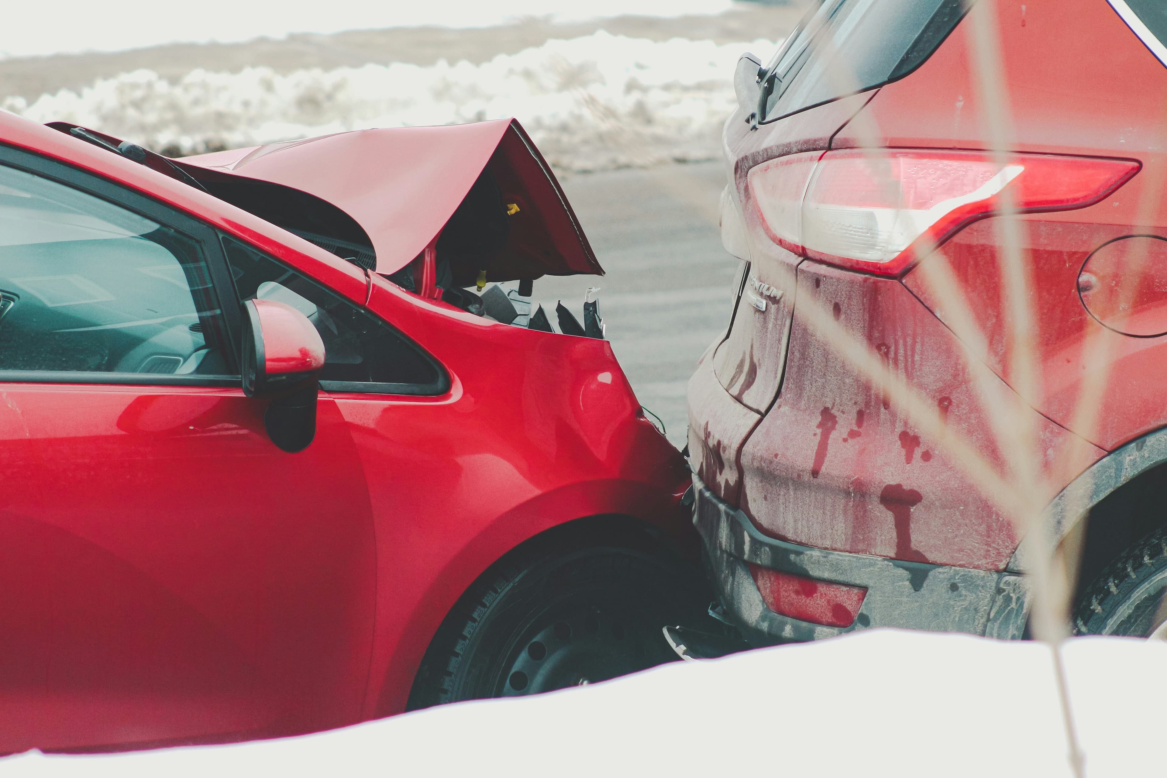 Two red cars in a rear-end collision on a snowy road